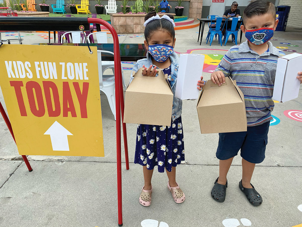 Two children in front of Kids Zone sign holding boxes