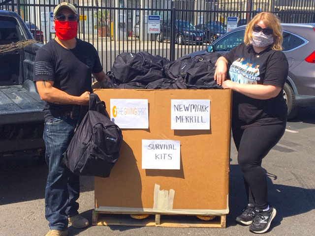Two volunteers standing next to large bin full of backpacks